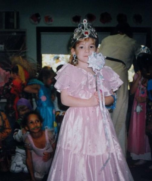 Ruth as a little girl. She's White and dressed in a pink princess dress with a crown and a wand.